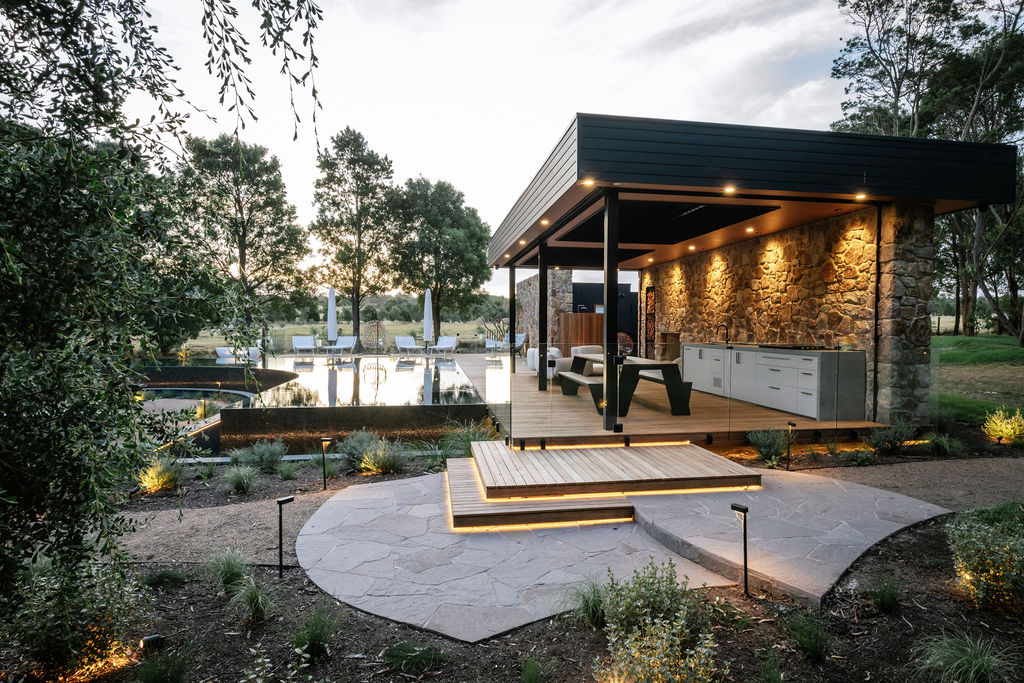 Dusk at the resort pool with illuminated outdoor lighting at deck, platform steps, in garden and in pool house